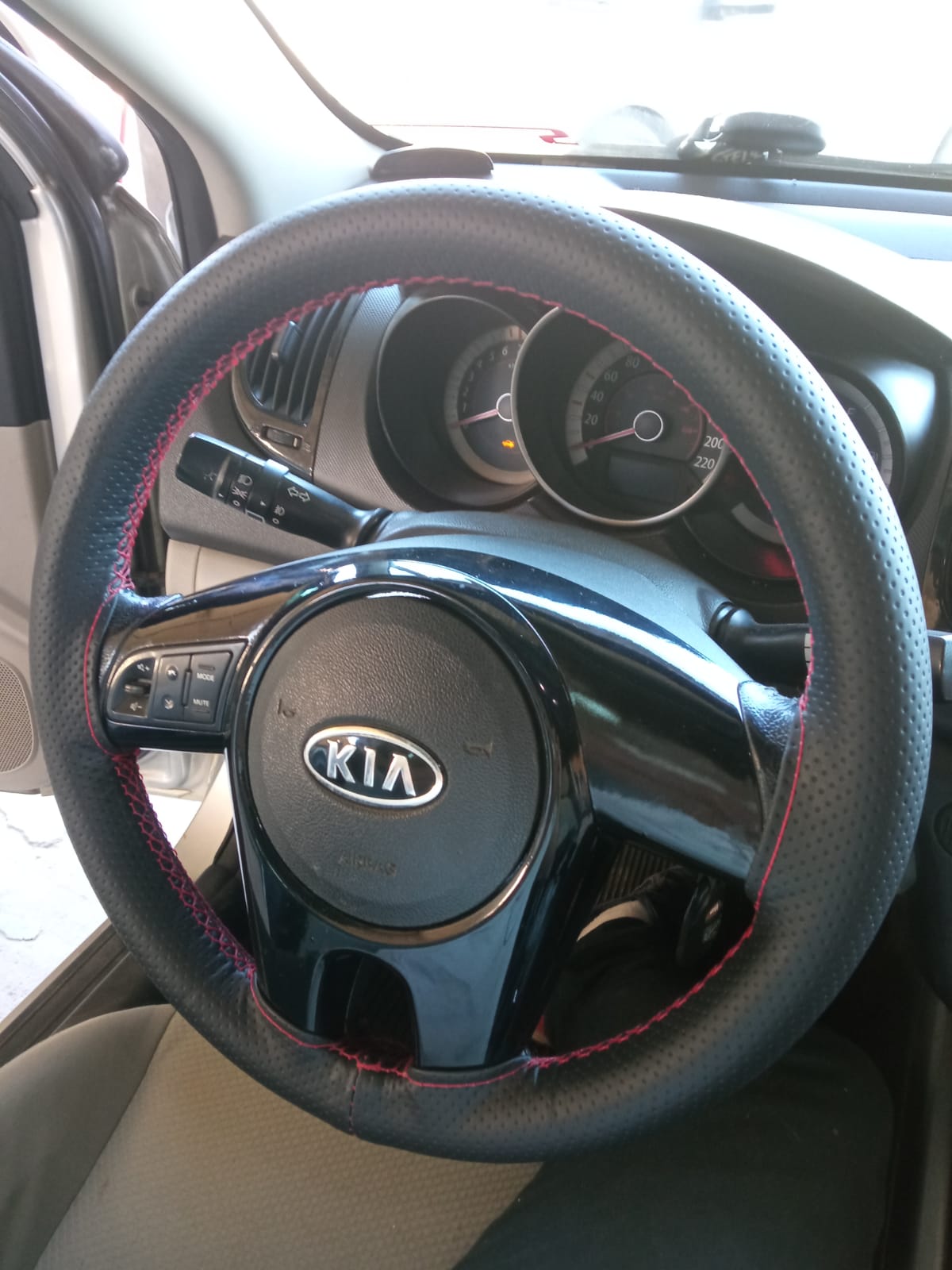 Volante de um carro da KIA com capa costurada e linha de costura vermelha.